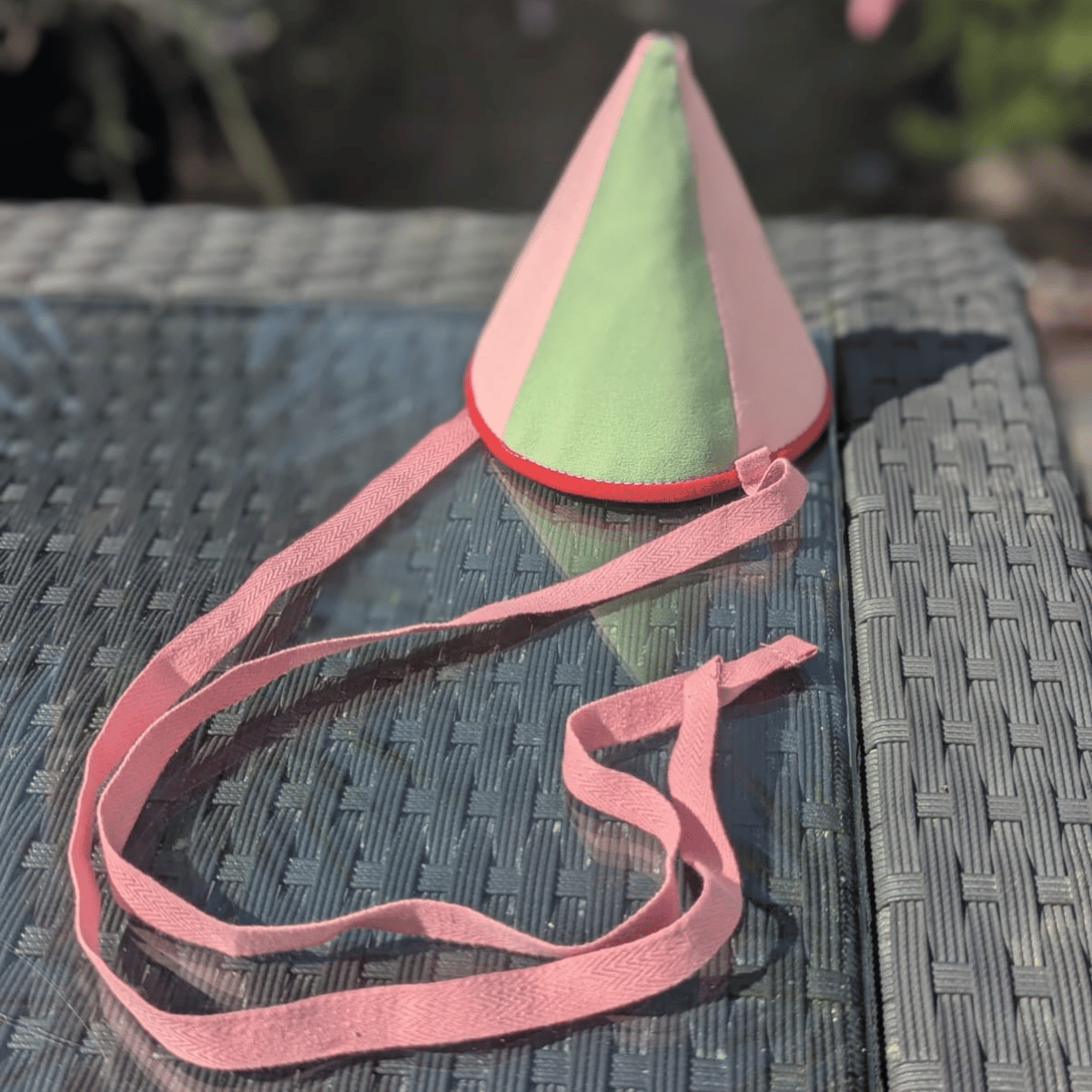 Green and pink cone-shaped hat with a pink strap on a textured surface